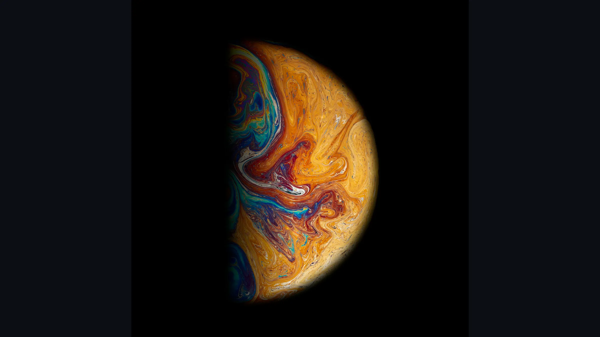 A sphere of swirling oil and pigment lit against black, its colours breaking from orange into blue.